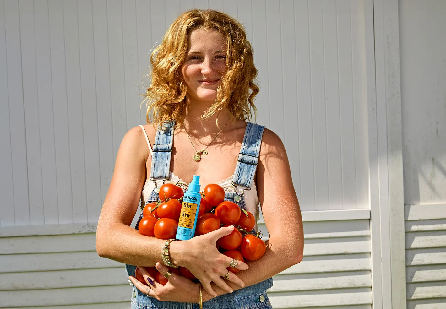 Woman holding a bundle of freshly picked tomatoes with a Mimikai bottle